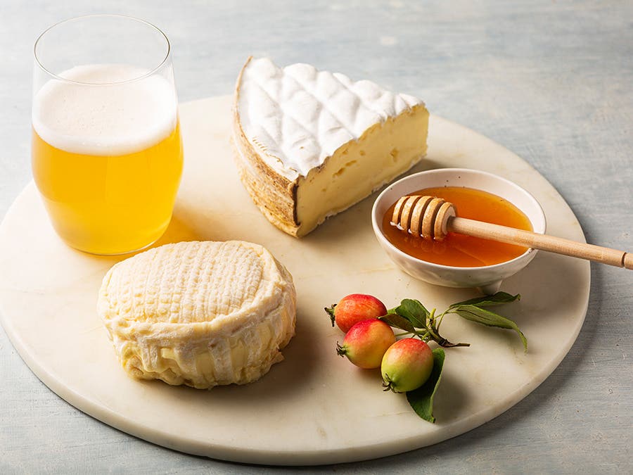 Un plateau avec deux fromages à pâte molle, un peu de miel et un verre de bière blanche