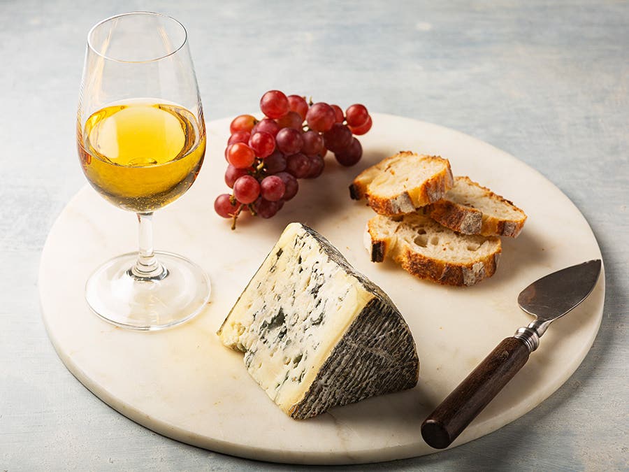 Un plateau avec un fromage bleu, des tranches de pain, des raisins rouges et un verre de cidre de glace